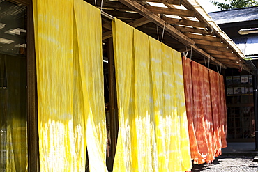 Freshly dyed bright yellow and orange fabric hanging outside a textile plant dye workshop, Kyushu, Japan