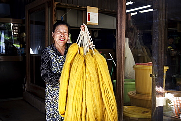 Japanese woman working in a plant dye workshop,  holding up freshly dyed bright yellow fabric, Kyushu, Japan