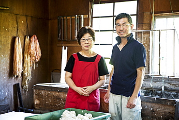 Japanese woman and man standing in a Washi workshop by a vat of pulp, basic plant based ingredients for making paper, Kyushu, Japan