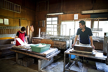 Two people, man and woman making traditional Washi paper. Trays of pulp and wooden frames and drying racks, Kyushu, Japan