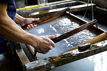 Japanese man in a workshop, holding a wooden frame with pressed pulp, making traditional Washi paper, Kyushu, Japan