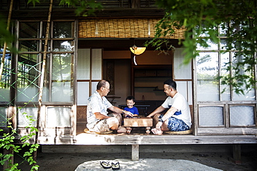 Two Japanese men and little boy sitting on floor on porch of traditional Japanese house, playing Go, Kyushu, Japan