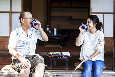 Japanese man and woman sitting on floor on porch of traditional Japanese house, drinking tea, Kyushu, Japan