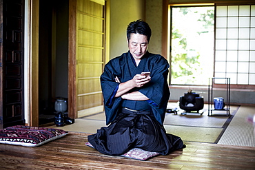 Japanese man wearing kimono sitting on floor in traditional Japanese house, using mobile phone, Kyushu, Japan