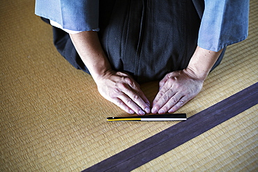 High angle close up of Japanese man kneeling on tatami mat in front of Sensu fan during a tea ceremony, used as a greeting, Kyushu, Japan