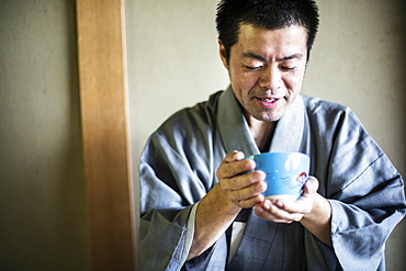 Japanese man wearing traditional kimono holding blue tea bowl during tea ceremony, Kyushu, Japan