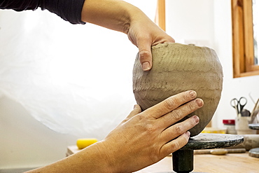 Close up of ceramic artist in her workshop, working on small clay vase, England