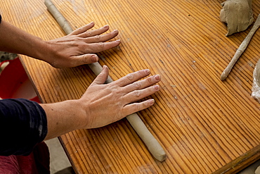 High angle close up of ceramic artist in her workshop, rolling out piece of clay on wooden table, England