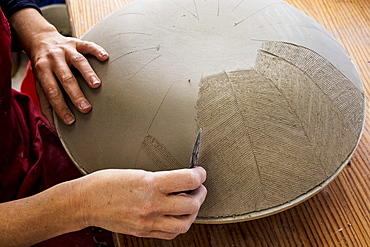 High angle close up of ceramic artist working on clay bowl, applying pattern with hand tool, England