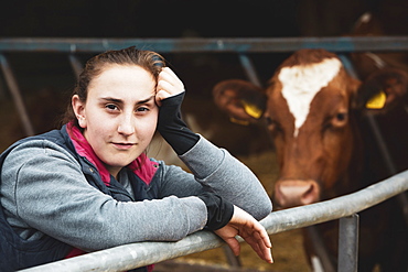 Young woman standing next to Guernsey cow on a farm, Oxfordshire, England