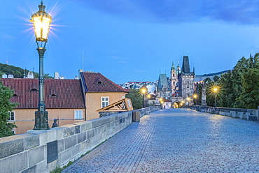 Illuminated streetlamps on cobblestone bridge at dawn, Prague, Czech Republic