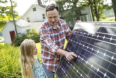 A man and a young girl looking at a solar panel in a garden.