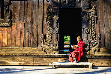 Asian monk reading by ornate doorway to temple