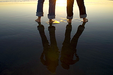 Reflection of legs in water at beach, Ventura, California, USA