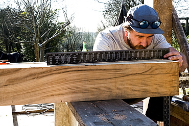 Man wearing baseball cap on building site, measuring wooden beam with metal ruler, Oxfordshire, England