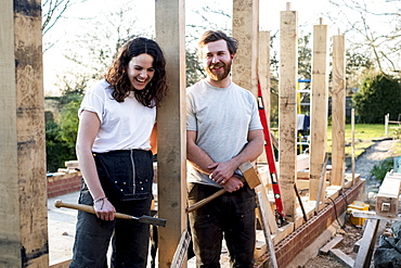 Smiling man and women holding hand tools standing on building site of residential building, Oxfordshire, England