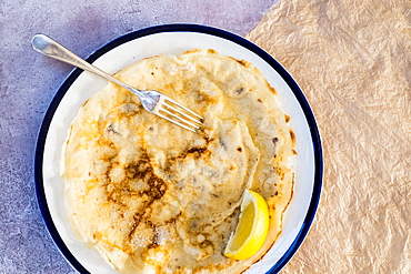 High angle close up of freshly baked crepe with lemon wedge garnish on white plate with blue rim, Oxfordshire, England