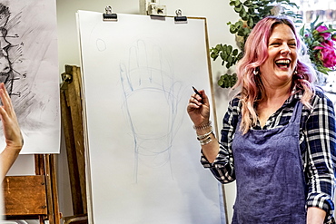 Laughing woman wearing apron standing at an easel, drawing of human hand, Oxfordshire, England