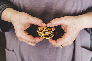 Close up of person holding small stack of freshly baked seeded crackers, England