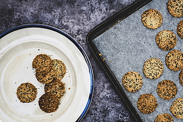 High angle close up of freshly baked seeded crackers on a plate and baking tray, England