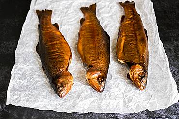 High angle close up of three freshly smoked whole trout on a white paper