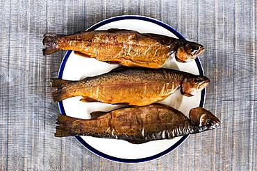 High angle close up of three freshly smoked whole trout on a white plate