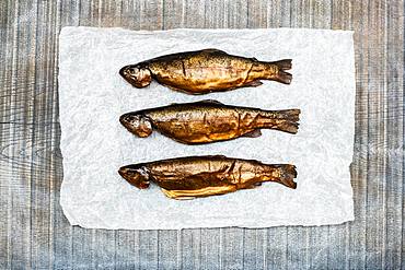 High angle close up of three freshly smoked whole trout on a white paper