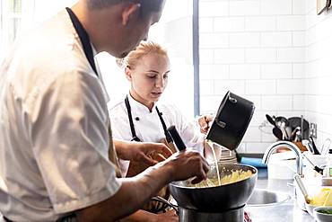 Male and female chef wearing brown aprons standing at kitchen counter, making Hollandaise Sauce