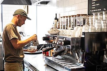 Bearded man wearing baseball cap standing at espresso machine a restaurant