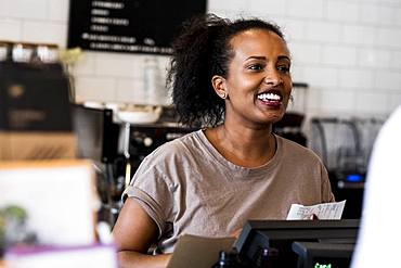 A woman barista smiling in welcome beside the counter in a coffee shop