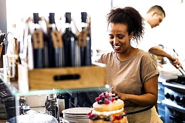 A woman working in a cafe, a stack of plates, and a layered sponge cake with fresh cream and fresh fruit