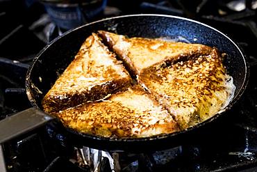 A frying pan on the hob, with eggy bread or croque monsieur sandwiches being fried