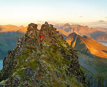 Man climbing up a steep peak in the jagged landscape of Senja Island, Troms, Senja Island, Lofoten Islands, Norway