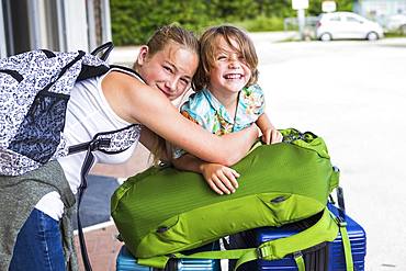 13 year old sister and her 5 year old brother leaning on travel luggage, Grand Cayman, Cayman Islands