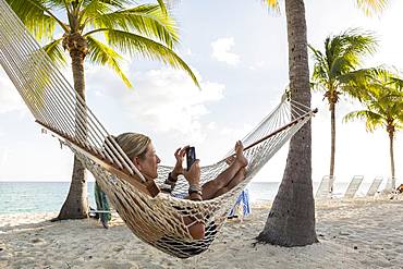 Woman in hammock using her smart phone, Grand Cayman, Cayman Islands