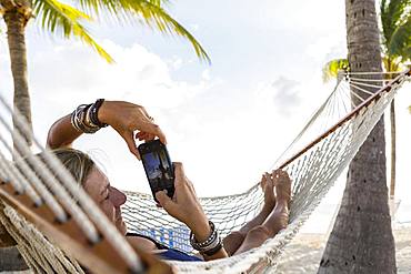 Woman in hammock using her smart phone, Grand Cayman, Cayman Islands