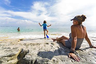 5 year old boy walking on rocks on the shore with swimming fins, Grand Cayman, Cayman Islands