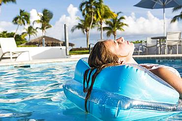 A teenage girl relaxing in a floatie in a pool, Grand Cayman, Cayman Islands