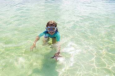 5 year old boy in the water holding a star fish, Grand Cayman, Cayman Islands