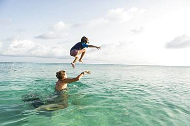 5 year old son on mother's shoulders leaping into the ocean at sunset, Grand Cayman, Cayman Islands