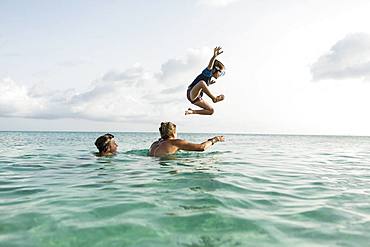 5 year old son on mother's shoulders leaping into the ocean at sunset, Grand Cayman, Cayman Islands