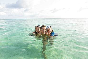 Adult woman standing in ocean water at sunset with her children, Grand Cayman, Cayman Islands