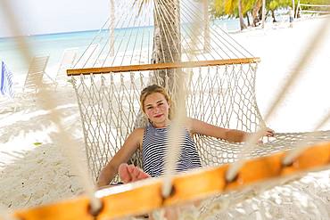 A teenage girl relaxing in a hammock on the beach, Grand Cayman, Cayman Islands