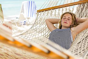 A teenage girl relaxing in a hammock on the beach, Grand Cayman, Cayman Islands