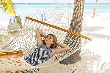 A teenage girl relaxing in a hammock on the beach, Grand Cayman, Cayman Islands