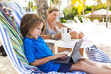 5 year old boy using laptop at the beach, Grand Cayman, Cayman Islands