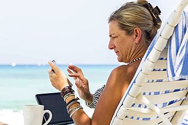 Adult woman executive using smart phone on the beach, Grand Cayman, Cayman Islands