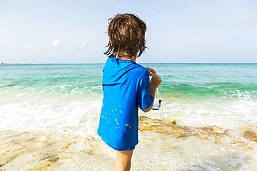 5 year old boy preparing to wear snorkelling mask, Grand Cayman, Cayman Islands