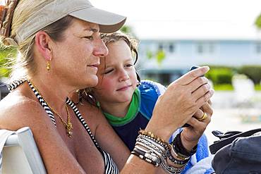 mother and 5 year old son looking at smart phone at the beach, Grand Cayman, Cayman Islands