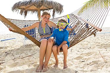 A teenage girl and her brother sitting on a hammock on the beach, Grand Cayman, Cayman Islands